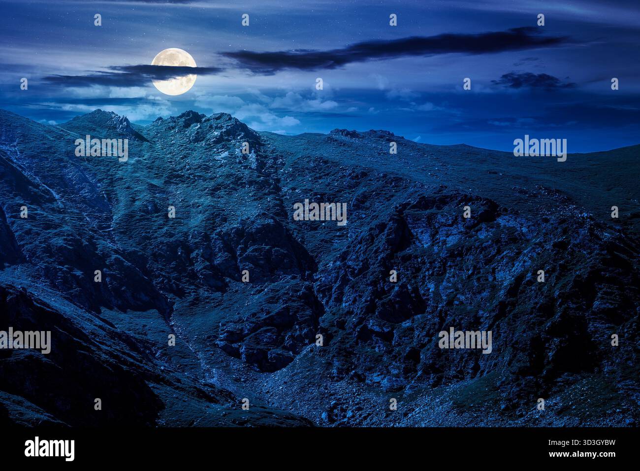 mountain landscape in summer at night. ridge under blue sky with clouds in full moon light. alpine scenery with rocky peaks and steep slopes. horizont Stock Photo