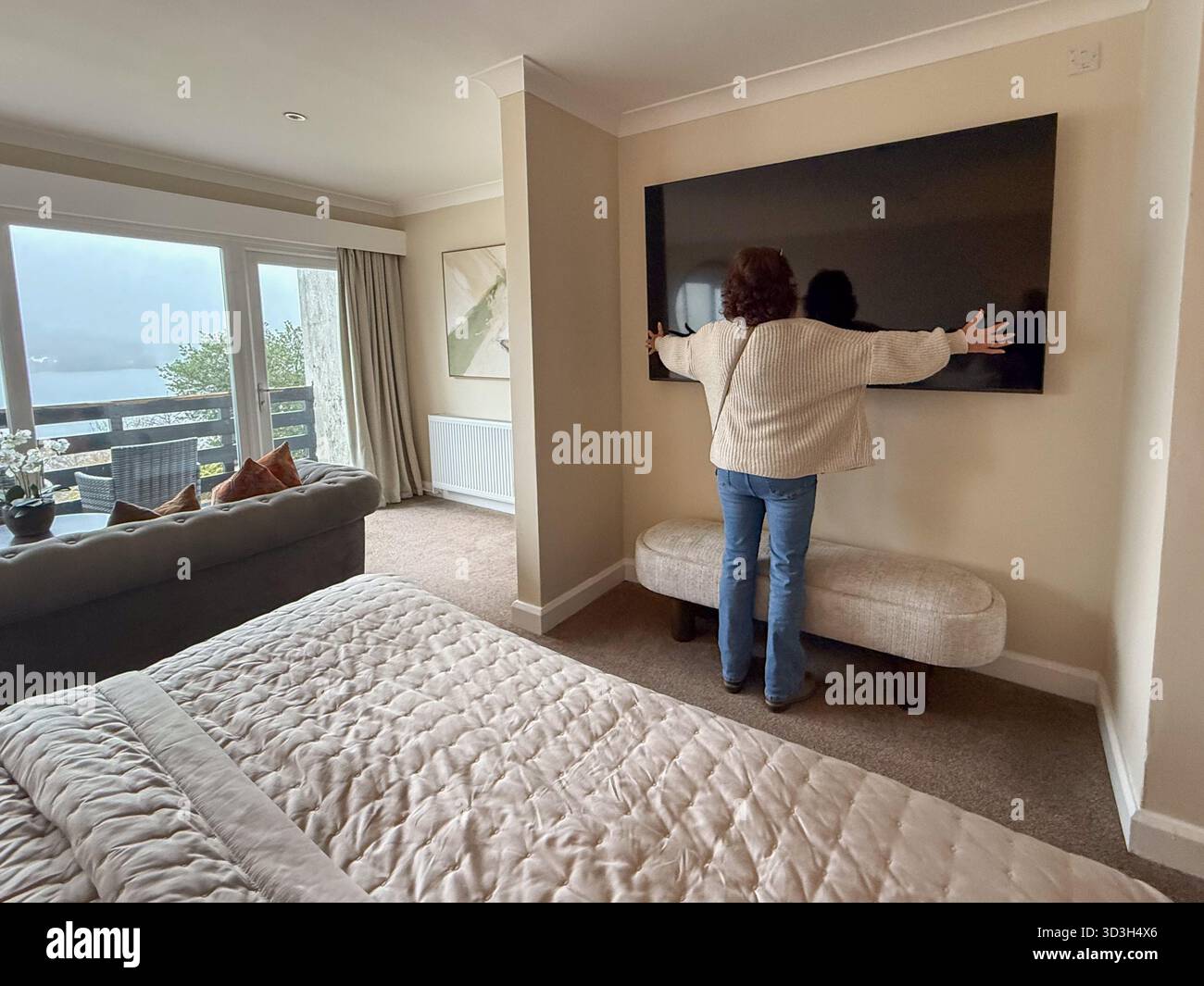 Woman measuring with outsretched arms a huge on wall tv in her hotel room at Beech Hill hotel and spa on lake windermere - Smartphone Captured Stock Image
