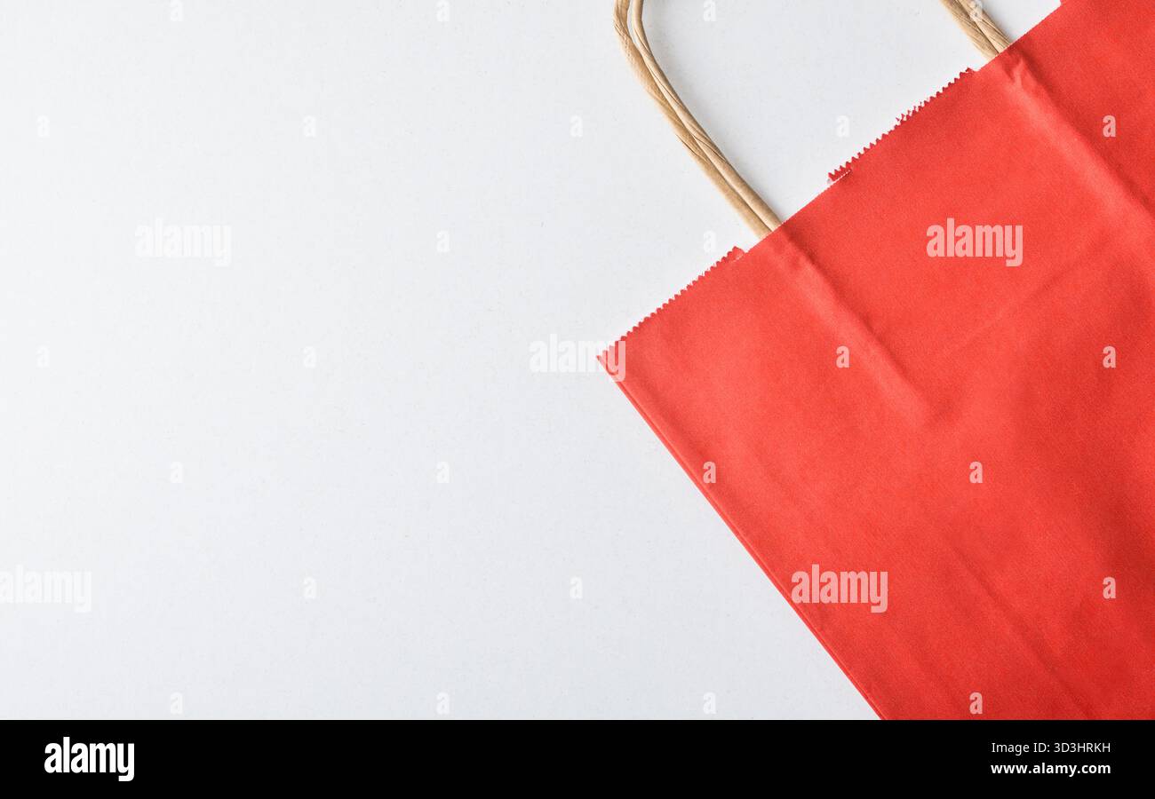 Detail of an empty, folded red paper shopping bag with brown braided paper handles on a white background. Top view. Stock Photo