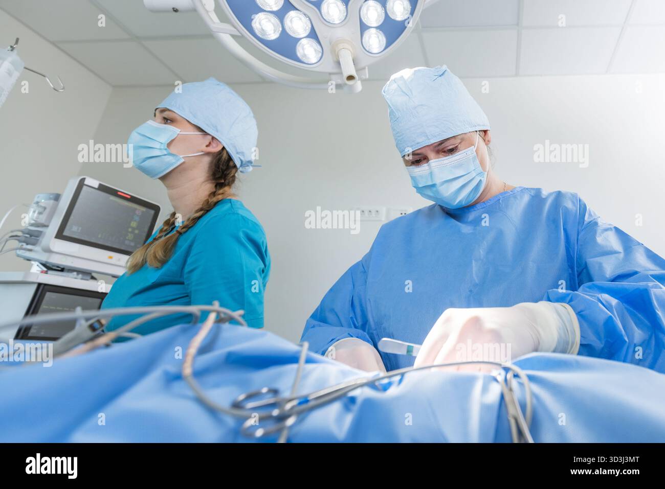 Two surgeons in blue scrubs and masks are focused on a surgical procedure in a well-lit clinic environment. Stock Photo