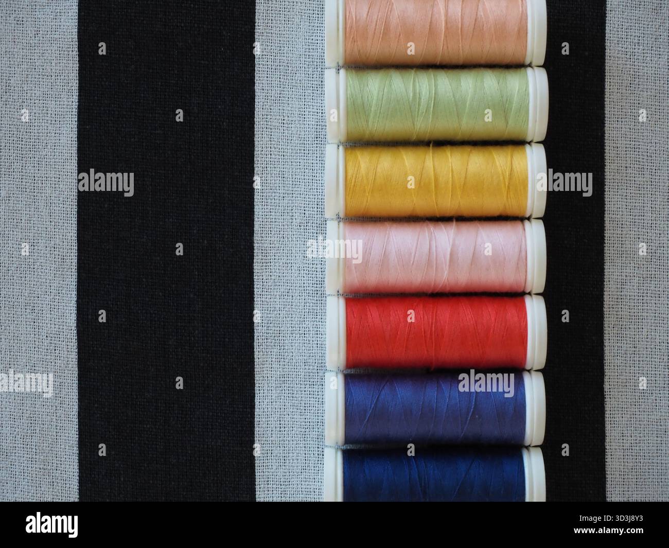 Top view of multicolored sewing threads on striped textile surface for fashion design and craft Stock Photo