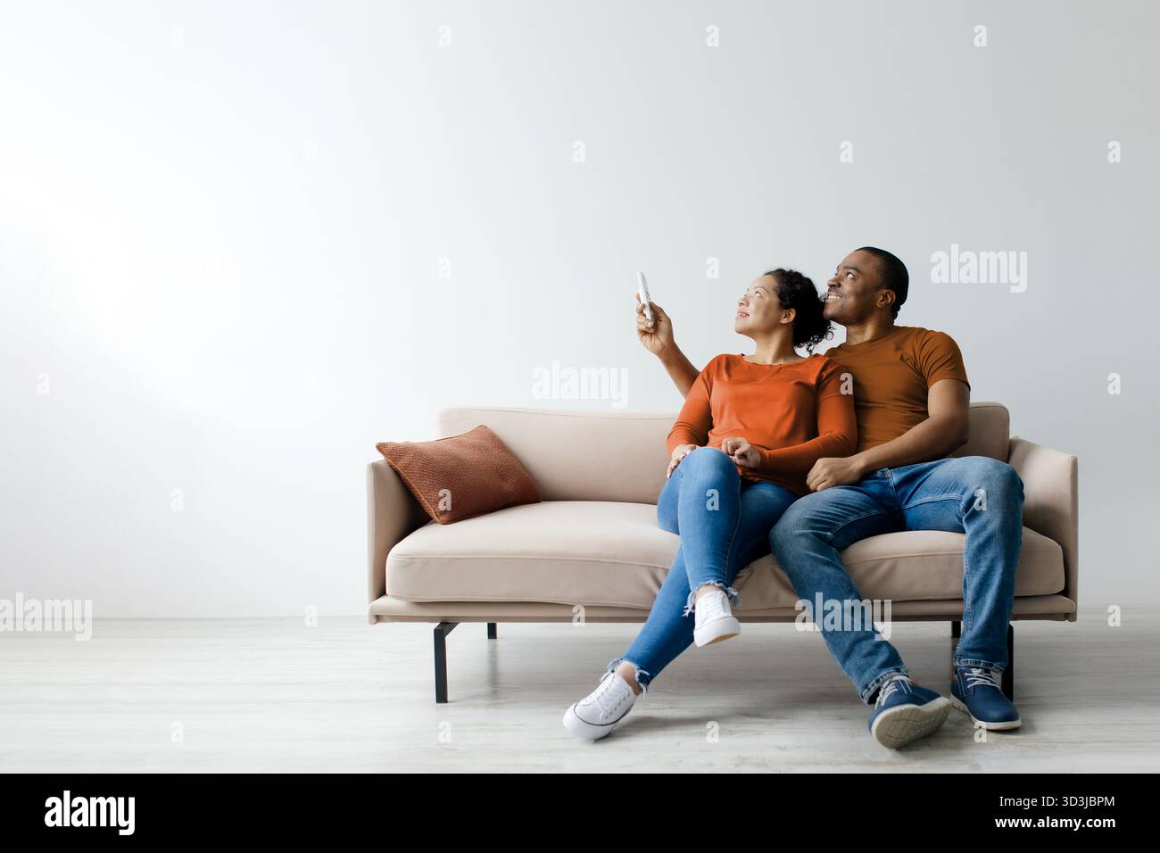 Split system. Cheerful young black couple opening air conditioner with remote Stock Photo