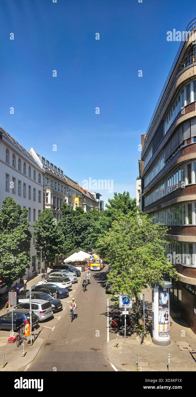 Berlin, Germany - May 13, 2025: Urban street scene features trees, modern buildings, and people walking in bright sunlight. - Smartphone Captured Stock Image