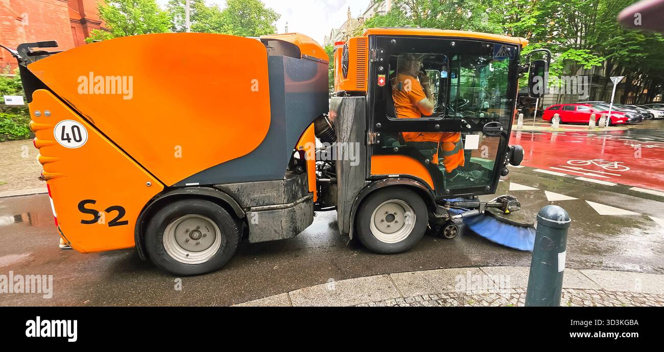 Berlin, Germany - June 05, 2025: Street cleaning machine is actively cleaning urban road with wet pavement. - Smartphone Captured Stock Image