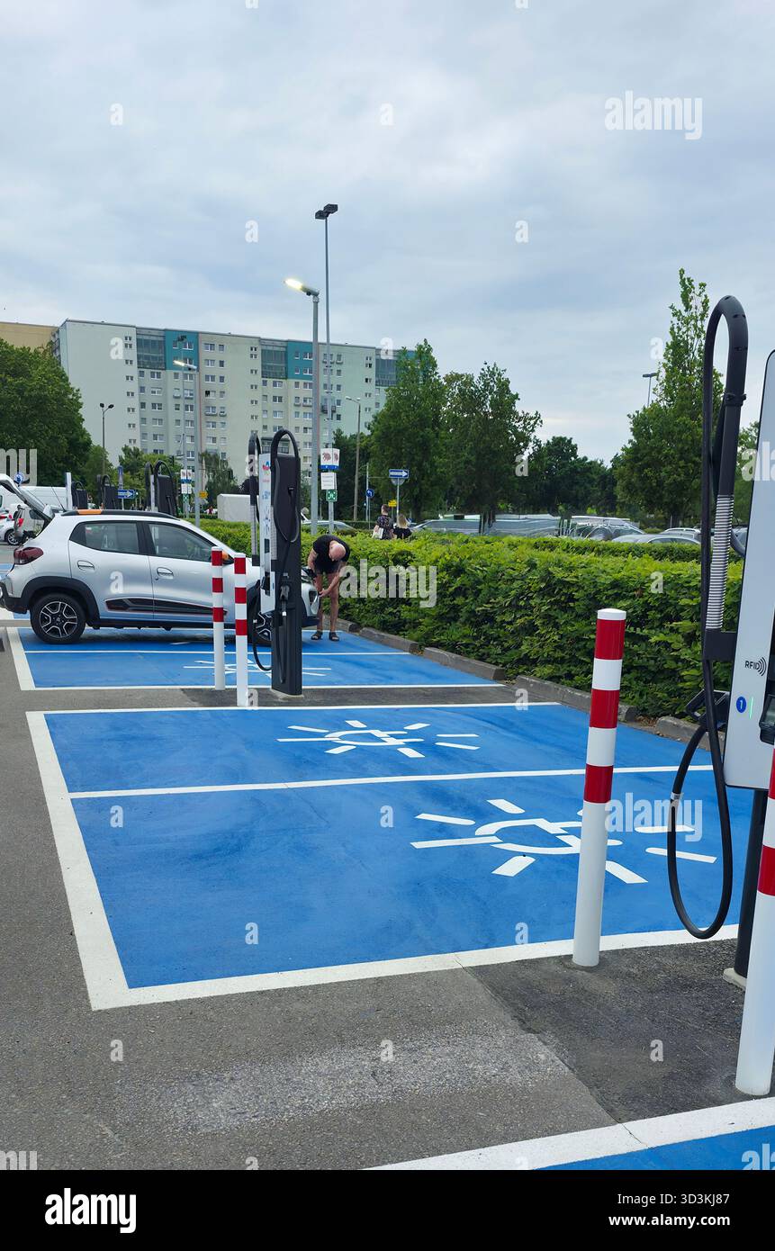 Berlin, Germany - June 28, 2025: Electric vehicle charging station features cars parked in urban area with greenery. - Smartphone Captured Stock Image