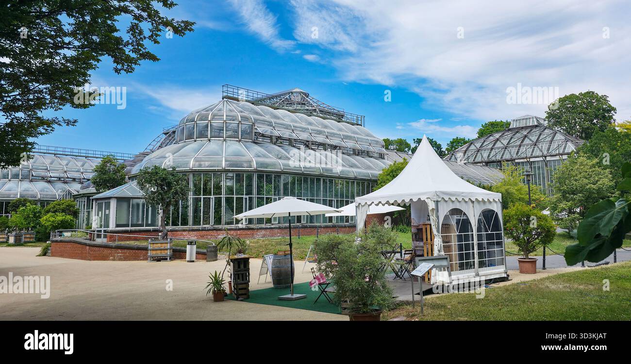 Berlin, Germany - July 03, 2025: . Greenhouse structure features outdoor seating area with white tent and lush greenery - Smartphone Captured Stock Image