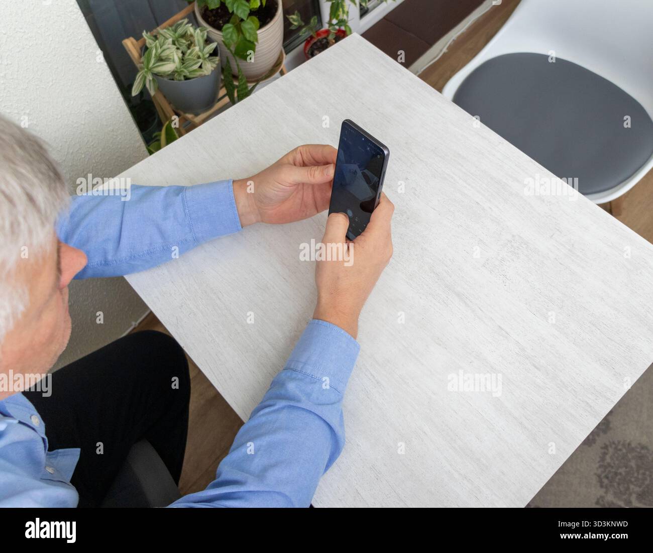 Mid aged man sitting at the table, using phone Stock Photo
