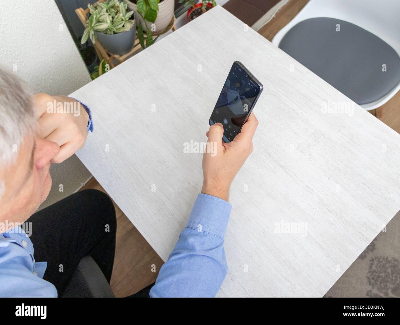 Mid aged man sitting at the table, using phone Stock Photo