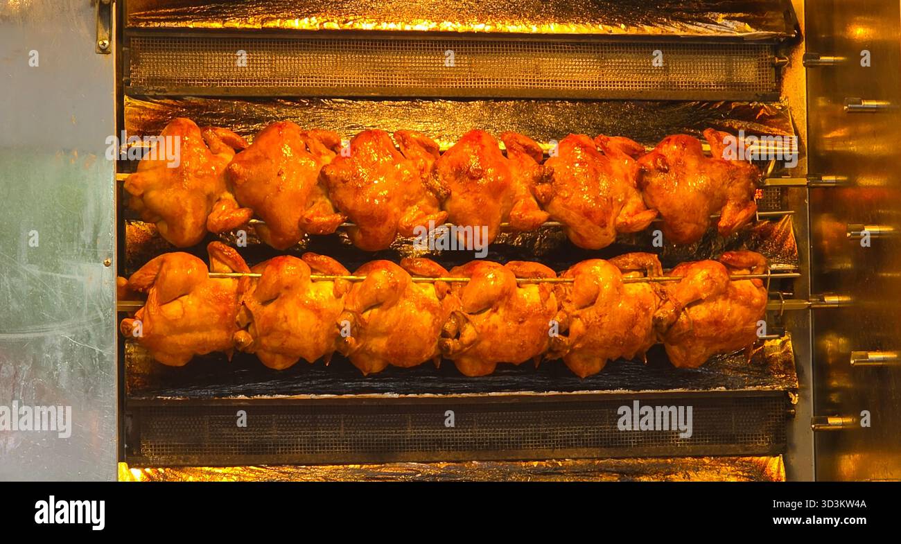 Roasted chickens are displayed on a rotating spit in a commercial kitchen, showcasing golden-brown skin and appetizing appearance. - Smartphone Captured Stock Image