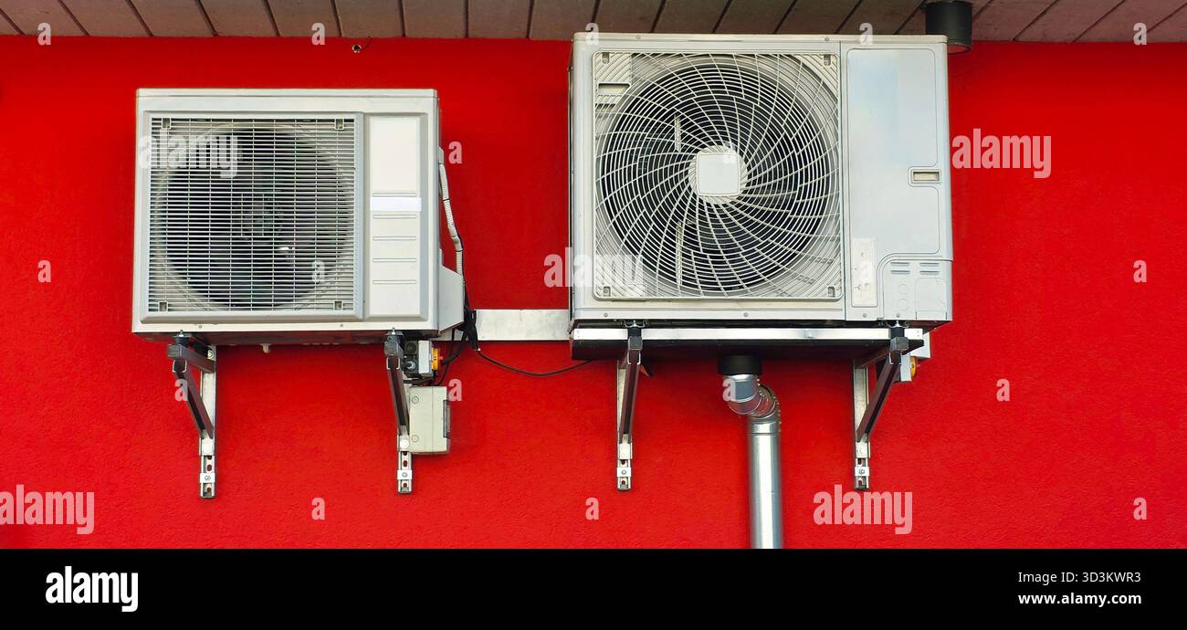 Air conditioning units are securely mounted on a wall, showcasing a vibrant red background, highlighting modern cooling technology and design. - Smartphone Captured Stock Image