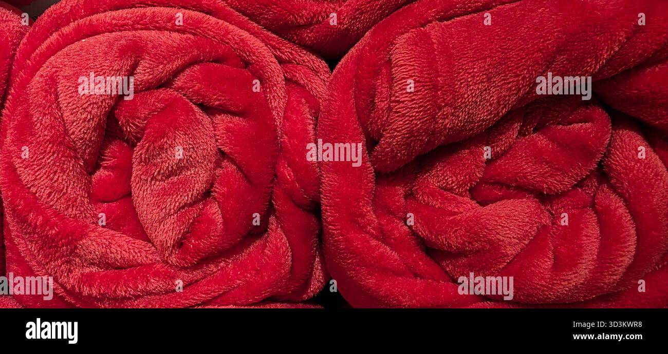 Soft red plush blankets are rolled up in a cozy arrangement, showcasing their texture and inviting warmth, perfect for a comfortable setting. - Smartphone Captured Stock Image