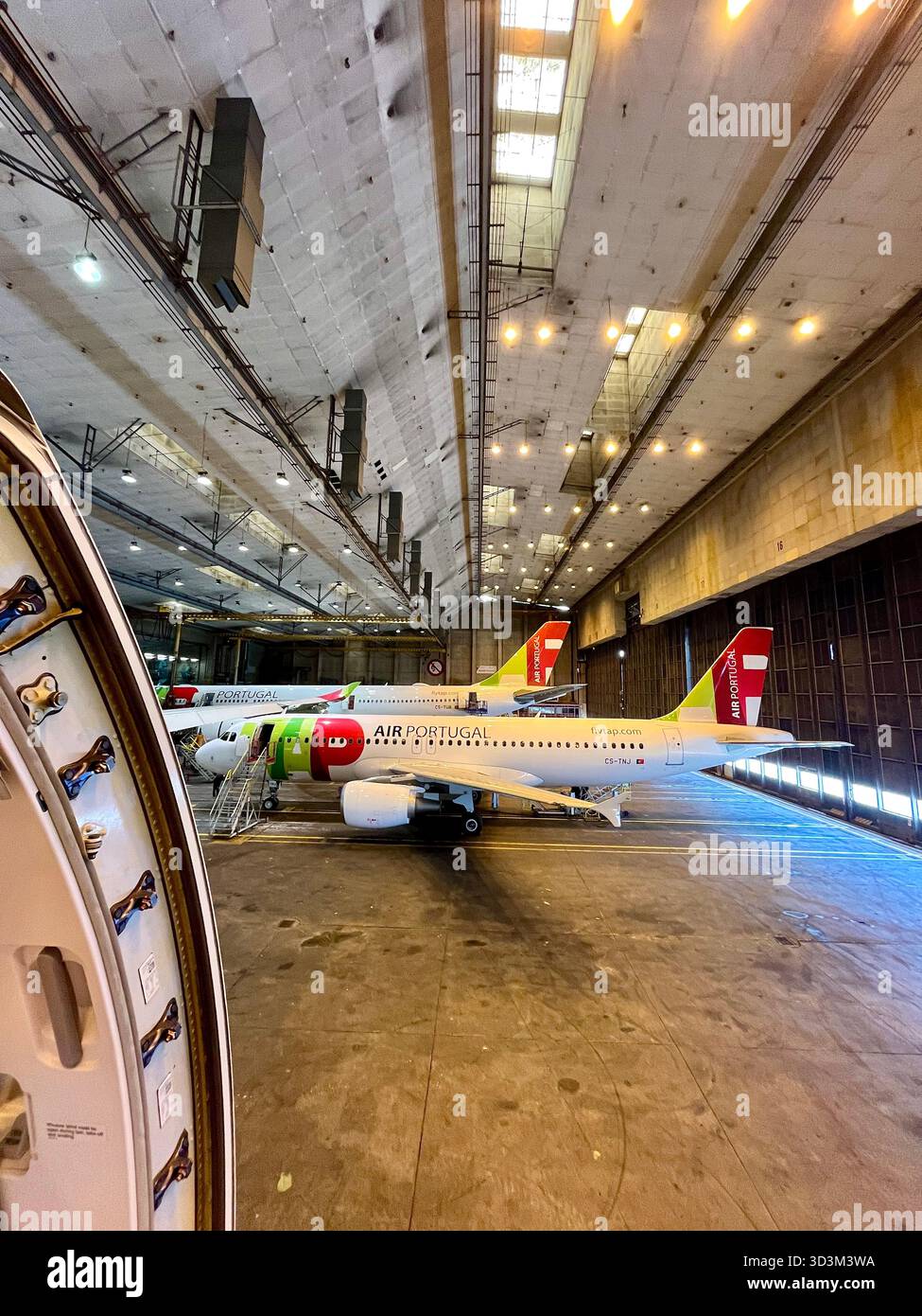 TAP Air Portugal aircraft undergoing maintenance inside large airline hangar with scaffolding and equipment visible. - Smartphone Captured Stock Image