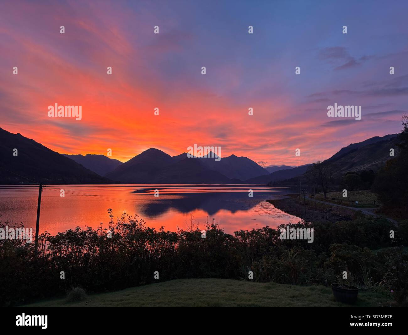 Brilliant orange and pink sunrise over Loch Duich in the Scottish Highlands, Scotland, with the mountains of the Five Sisters of Kintail reflected. - Smartphone Captured Stock Image