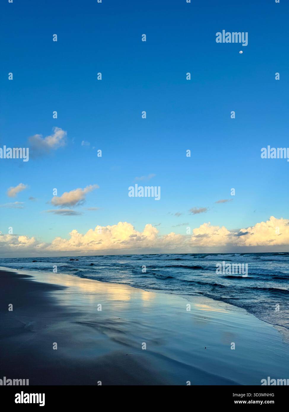 Peaceful morning at Praia do flamengo in Salvador, Brazil, with soft waves, golden light reflecting on the wet sand,and the moon visible in the sky. - Smartphone Captured Stock Image