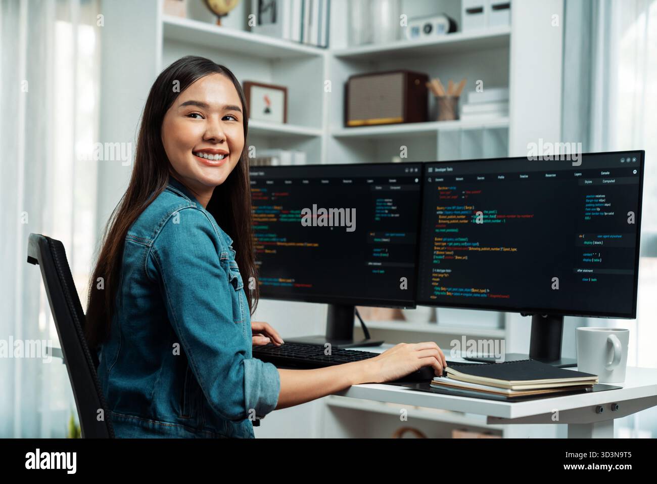 Young Asian in IT developer looking at camera to present with online information on pc with coding program data application, wearing jeans shirt Stock Photo