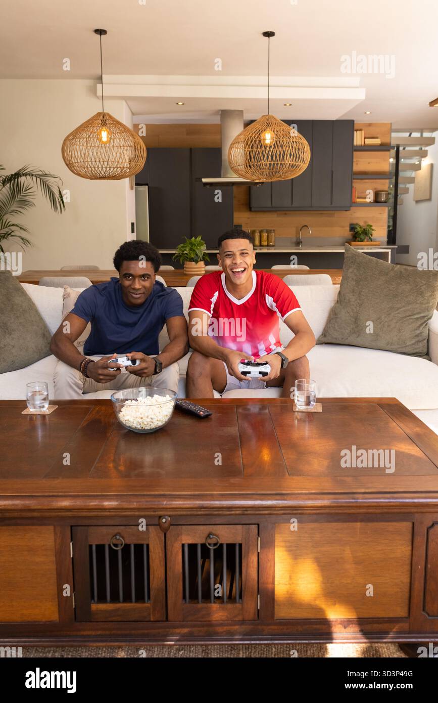 Playing diverse male friends sitting on couch in modern living room ...