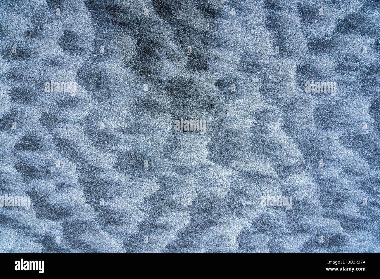 An abstract close-up view of rippled sand patterns, creating a mesmerizing texture. The natural blue-gray hue evokes a sense of tranquility and organi Stock Photo