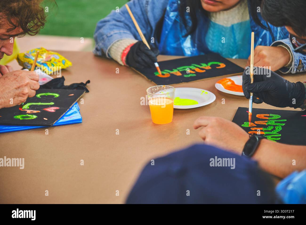Lima, peru. 01 november 2025: hands painting words with vibrant neon colors on black boards at a workshop Stock Photo