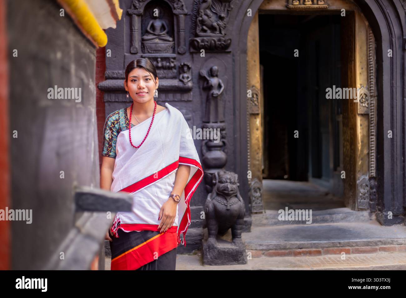 Grace in Heritage: Newari Girl in traditional attire at golden temple stone gate at Patan Durbar Square Stock Photo