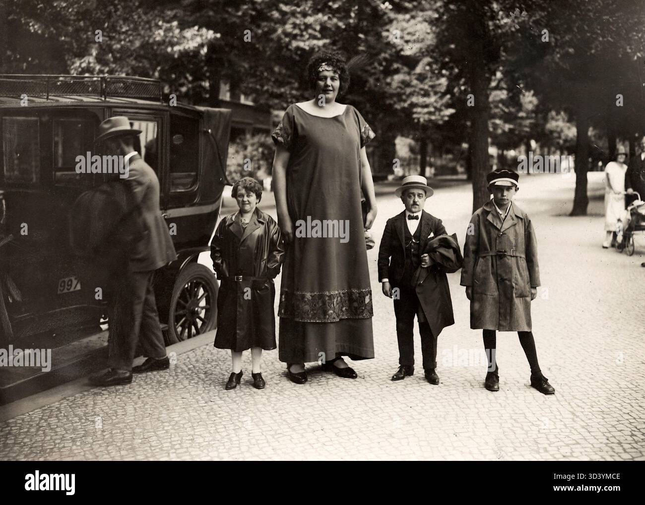 In 1925, tall woman 'Lange Kaatje' from Roosendaal stands among three 'lilliput' people in an unusual photograph. The contrasting heights highlight the differences between them. Stock Photo