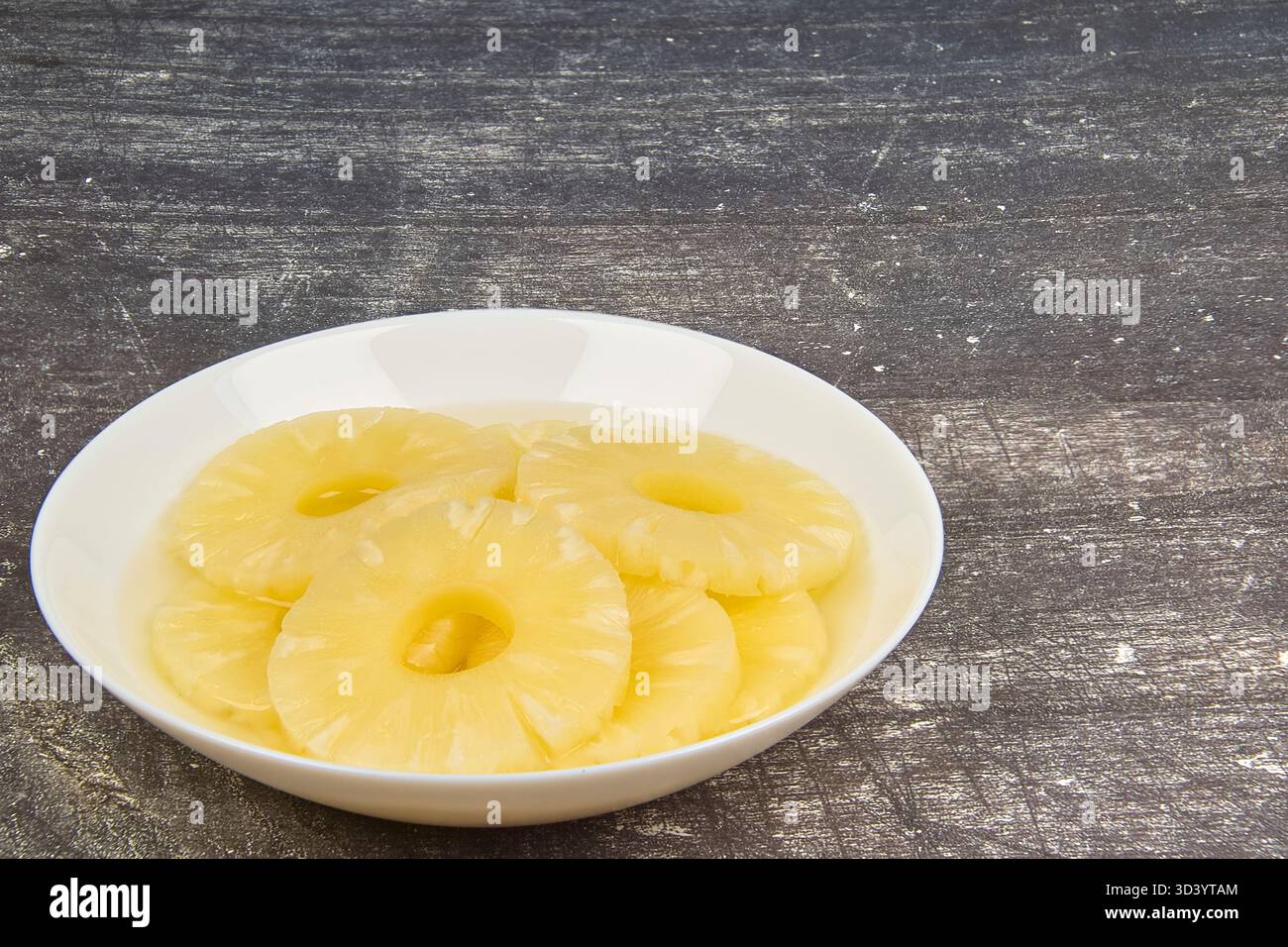 Sliced ​​pineapple, canned preserve. Close-up photograph with copy space on a table against a rustic background. Stock Photo