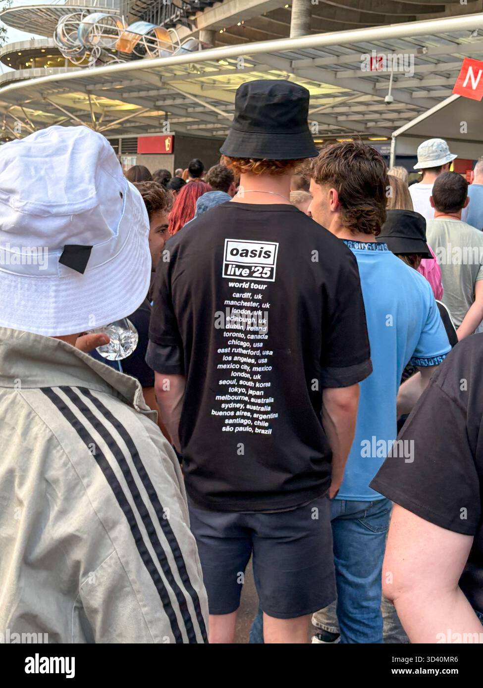 Oasis Live 25 tour, Sydney Accor Stadium, Oasis fans wearing bucket hat and Oasis tee shirt queue to enter Accor Stadium for 1st night in Sydney - Smartphone Captured Stock Image