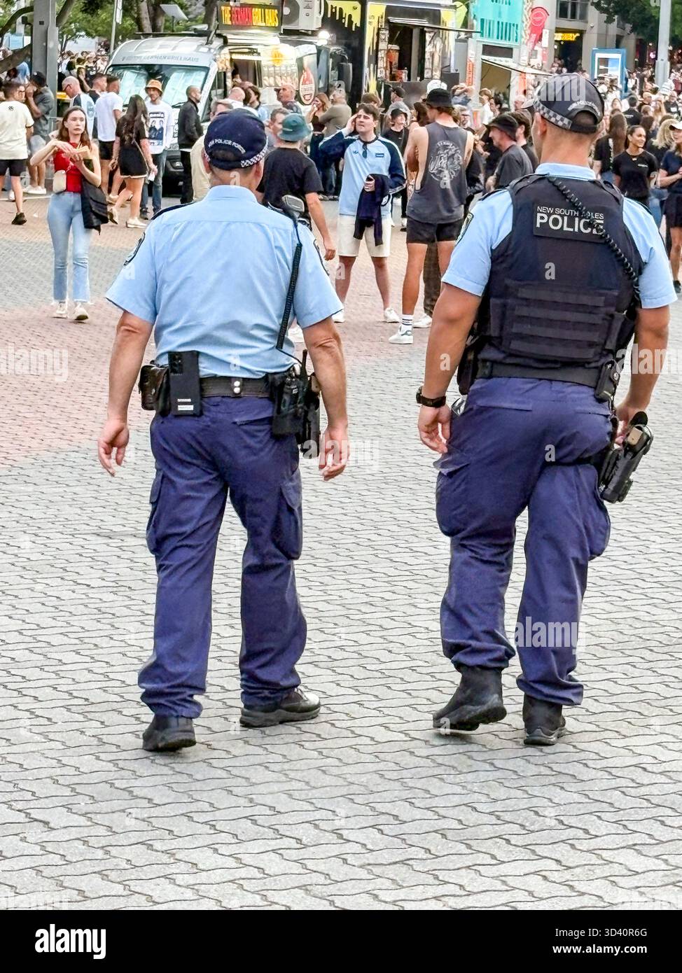 Australian police officers, two male New South Wales NSW policemen patrol the crowds outside the Accor  Stadium before the Oasis Live 25 concert - Smartphone Captured Stock Image