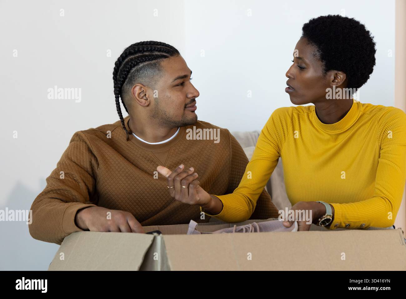Diverse couple opening large cardboard box on sofa in living room, with packing material Stock Photo