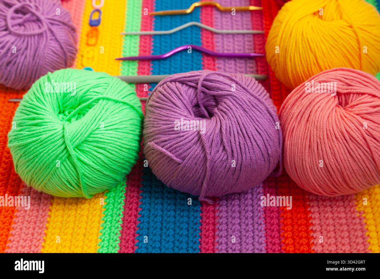 All for hand knitting. Knitted multi-colored handmade fabric with balls of multi-colored threads, pins and various knitting needles on it. Stock Photo