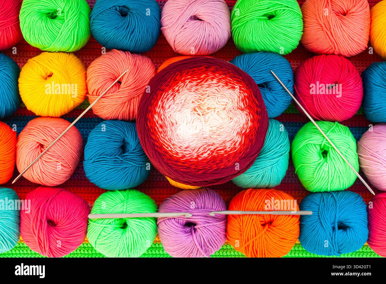 All for hand knitting. Knitted multi-colored handmade fabric with balls of multi-colored threads, pins and various knitting needles on it. Stock Photo