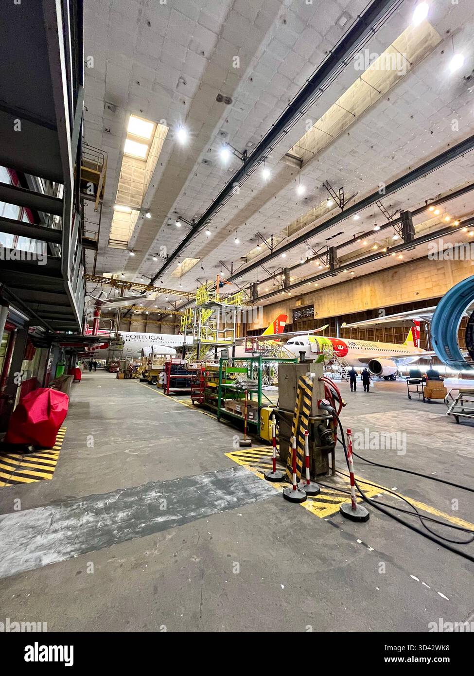 TAP Air Portugal Airbus aircraft undergoing maintenance inside a large engineering hangar with industrial equipment and scaffolding. - Smartphone Captured Stock Image