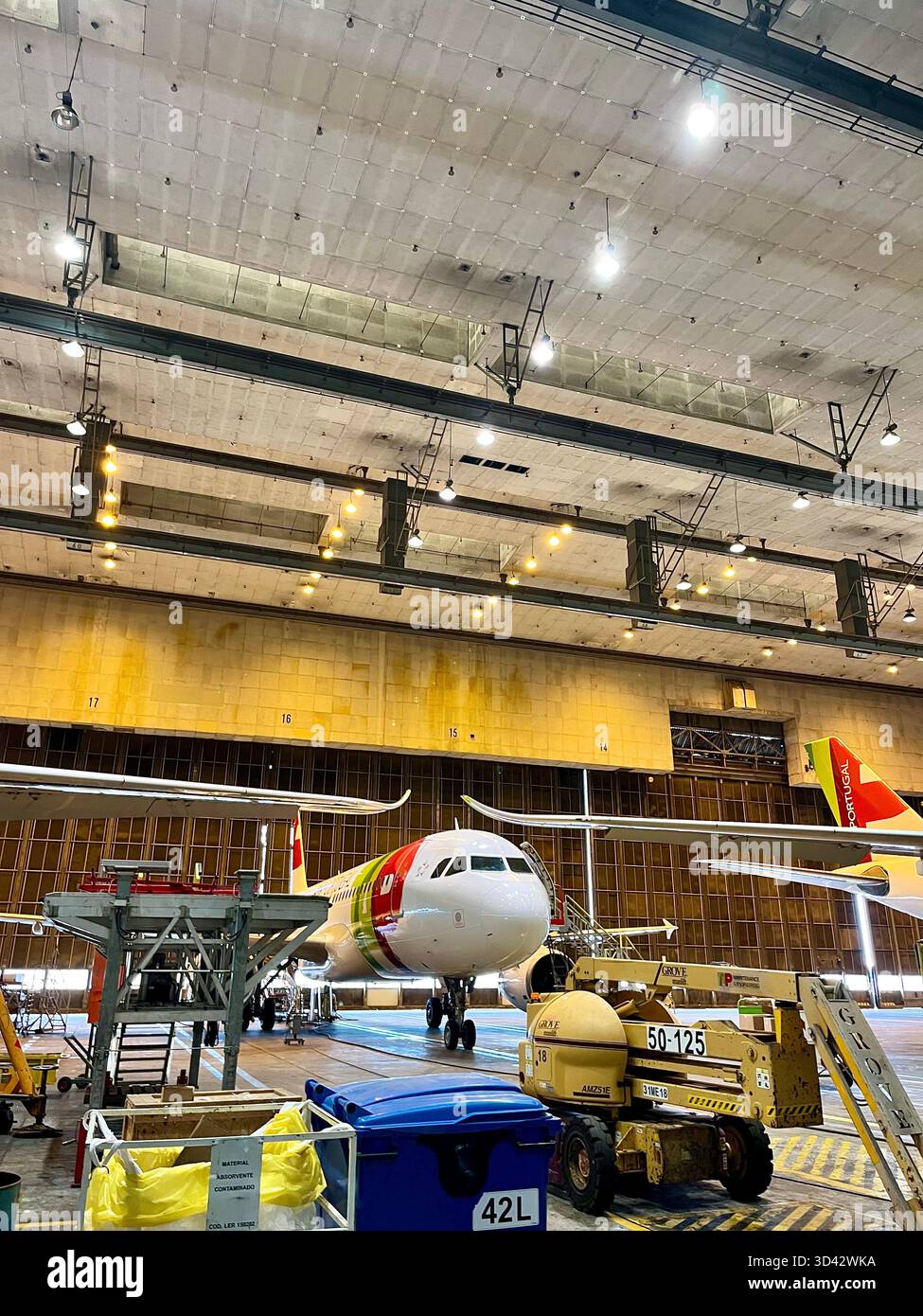TAP Air Portugal Airbus aircraft undergoing maintenance inside a large engineering hangar with industrial equipment and scaffolding. - Smartphone Captured Stock Image
