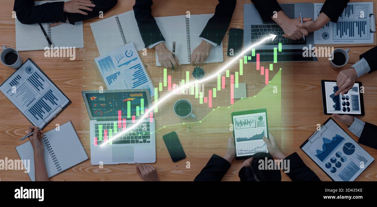 A business team collaborates in a meeting room, analyzing financial data on laptops and tablets, highlighting trends with charts and graphs for Stock Photo
