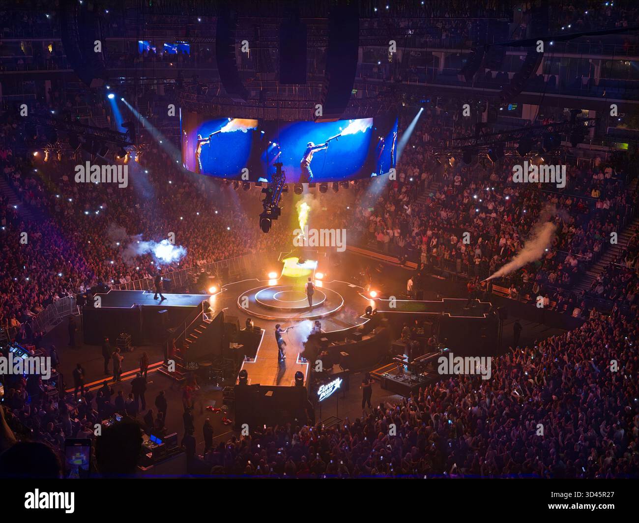 A crowded concert arena at night with bright stage lights and a large audience surrounding a central stage inside an ice palace. - Smartphone Captured Stock Image