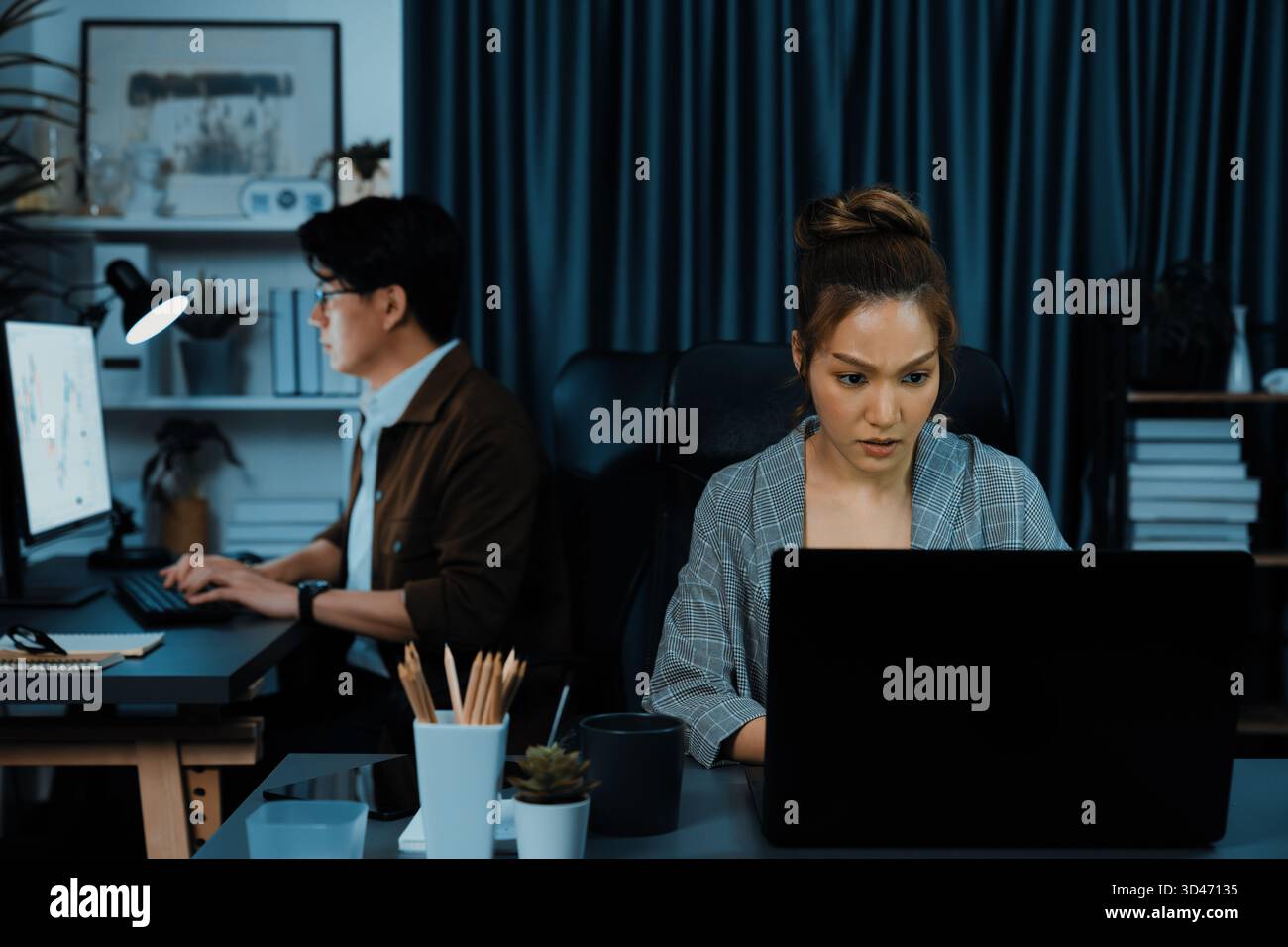 Serious face of thinking businesswoman focusing computer to report data analysis social media online project job with coworker working at back side at Stock Photo