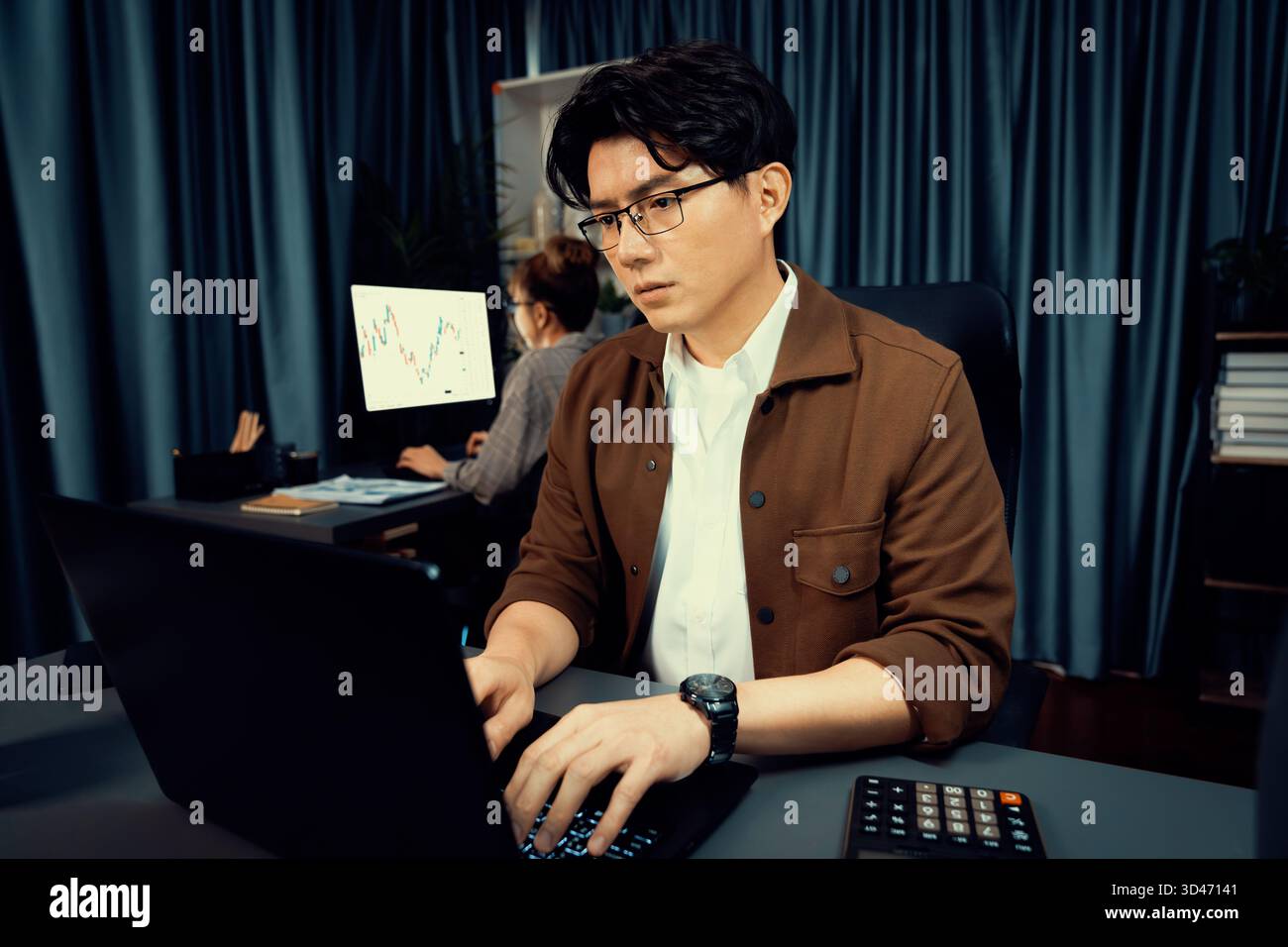 Serious face of thinking businessman focusing laptop to report data analysis social media online project with coworker analyzing stock at back side at Stock Photo