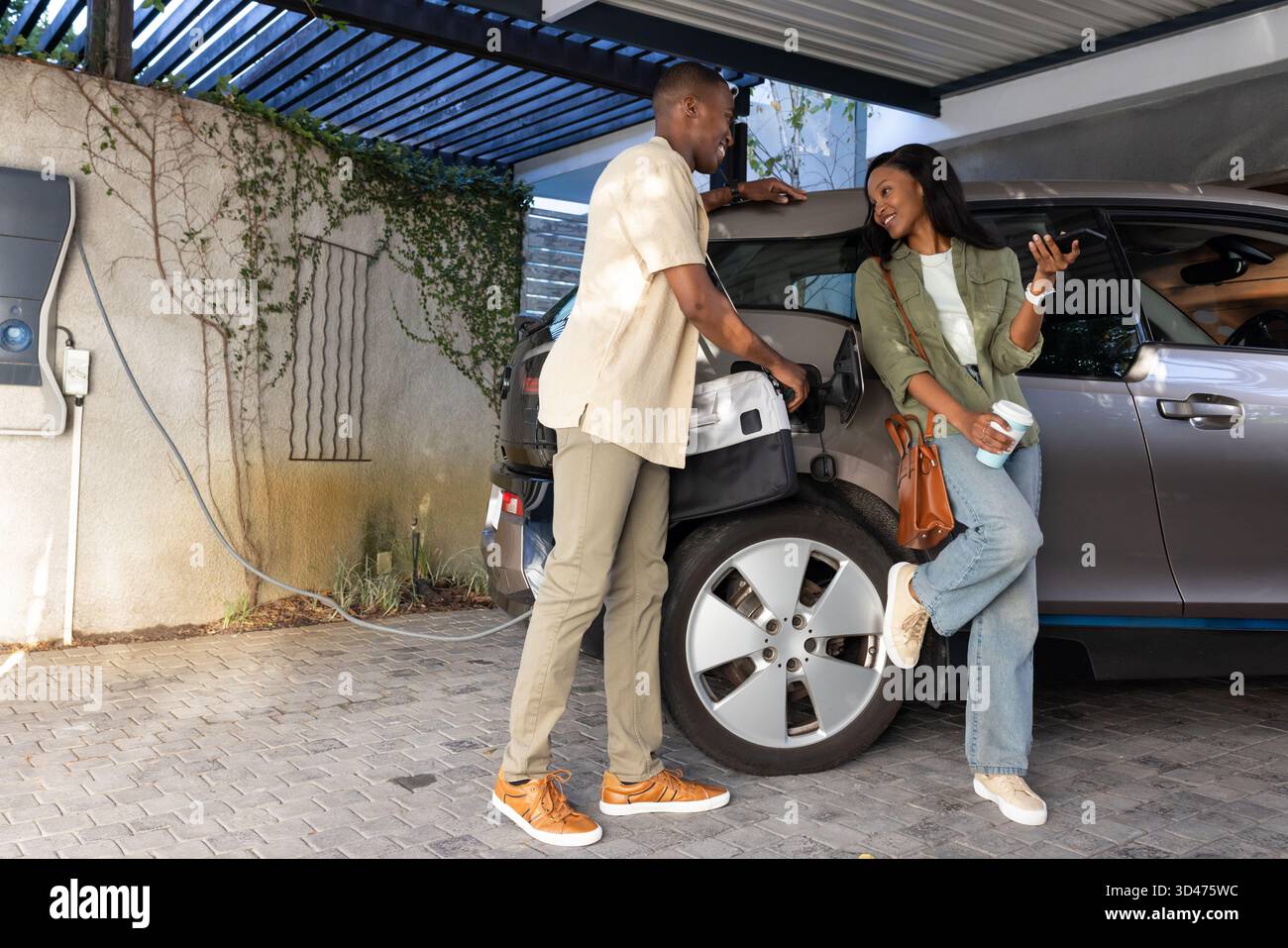 Plugging African American friends connecting charging cable under carport, with coffee cup phone Stock Photo