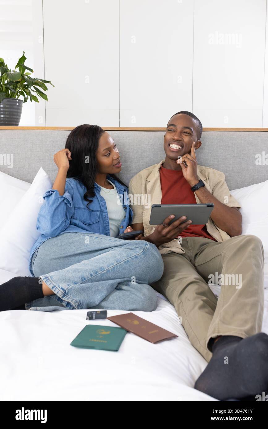 Browsing African American couple leaning on bed in bedroom, using ...