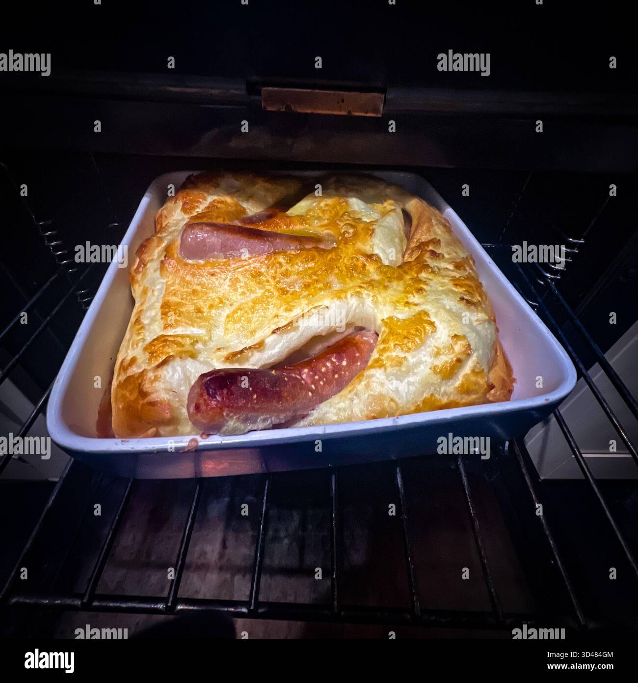 A toad in the hole being taken out of the oven. Toad in the hole is a classic British comfort dish: sausages baked in a light, airy Yorkshire pudding - Smartphone Captured Stock Image