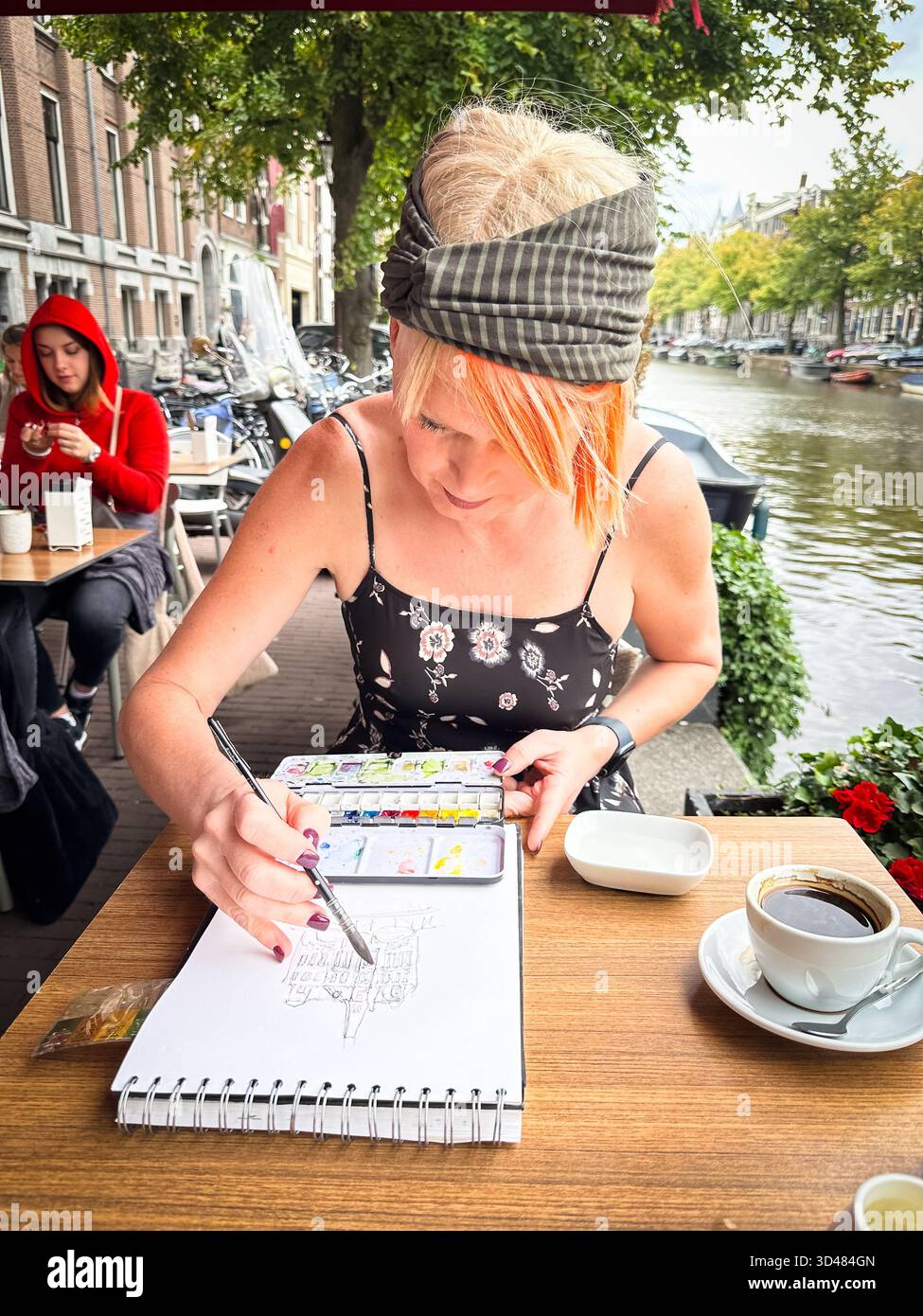 A female artist painting a watercolour on a cafe table in Amsterdam - Smartphone Captured Stock Image