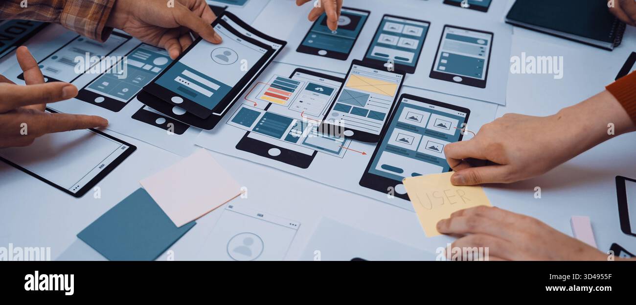 A dynamic workspace showcases hands engaged in a collaborative design process, creating mobile app prototypes and wireframes, reflecting teamwork and Stock Photo