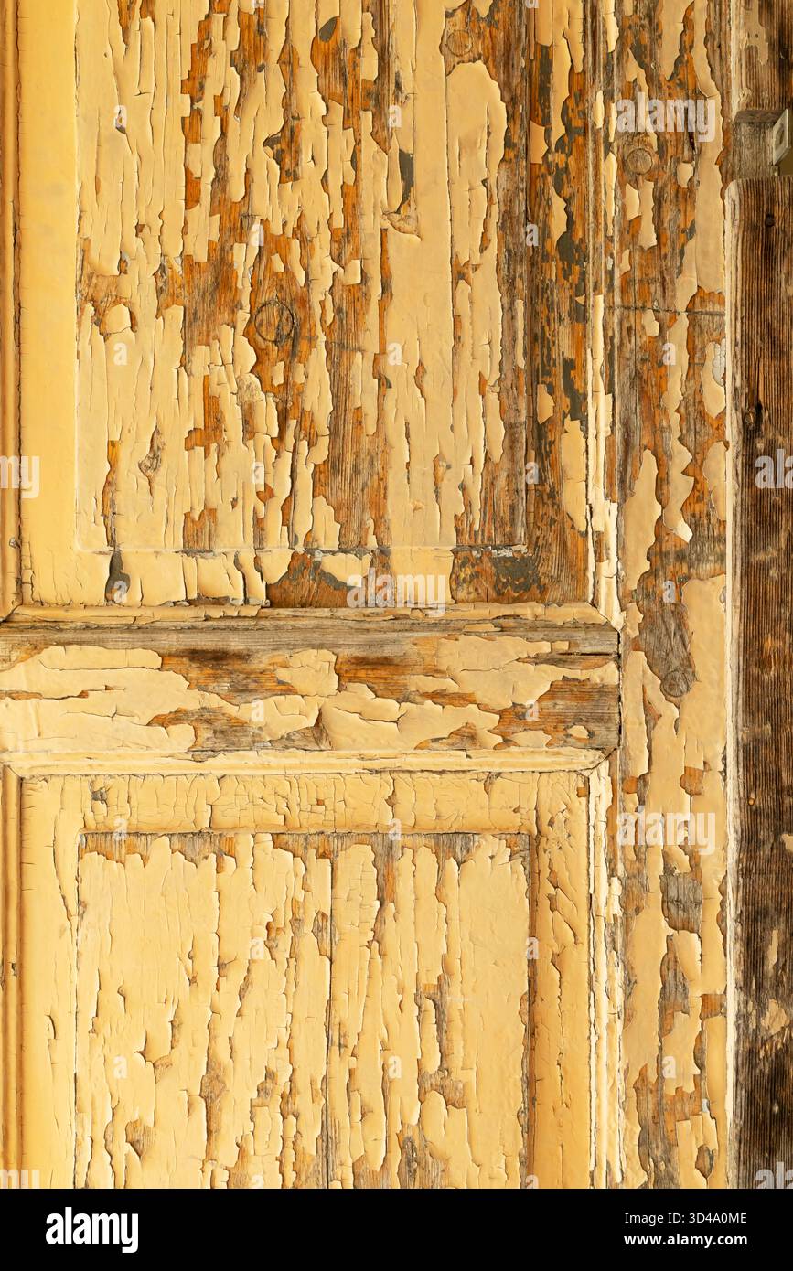 Peeling yellow paint on weathered wooden door creating rustic texture Stock Photo