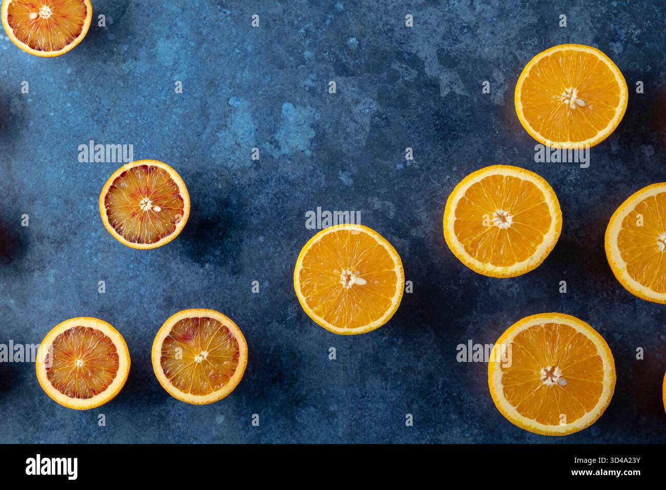 Sliced citrus fruit including oranges and blood oranges on a blue textured surface Stock Photo