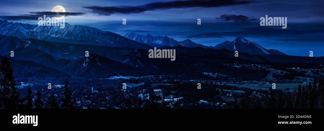 panorama of Mountain range in summer at night. village in the valley in full moon light. clouds on the sky and rolling hills. background for investmen Stock Photo
