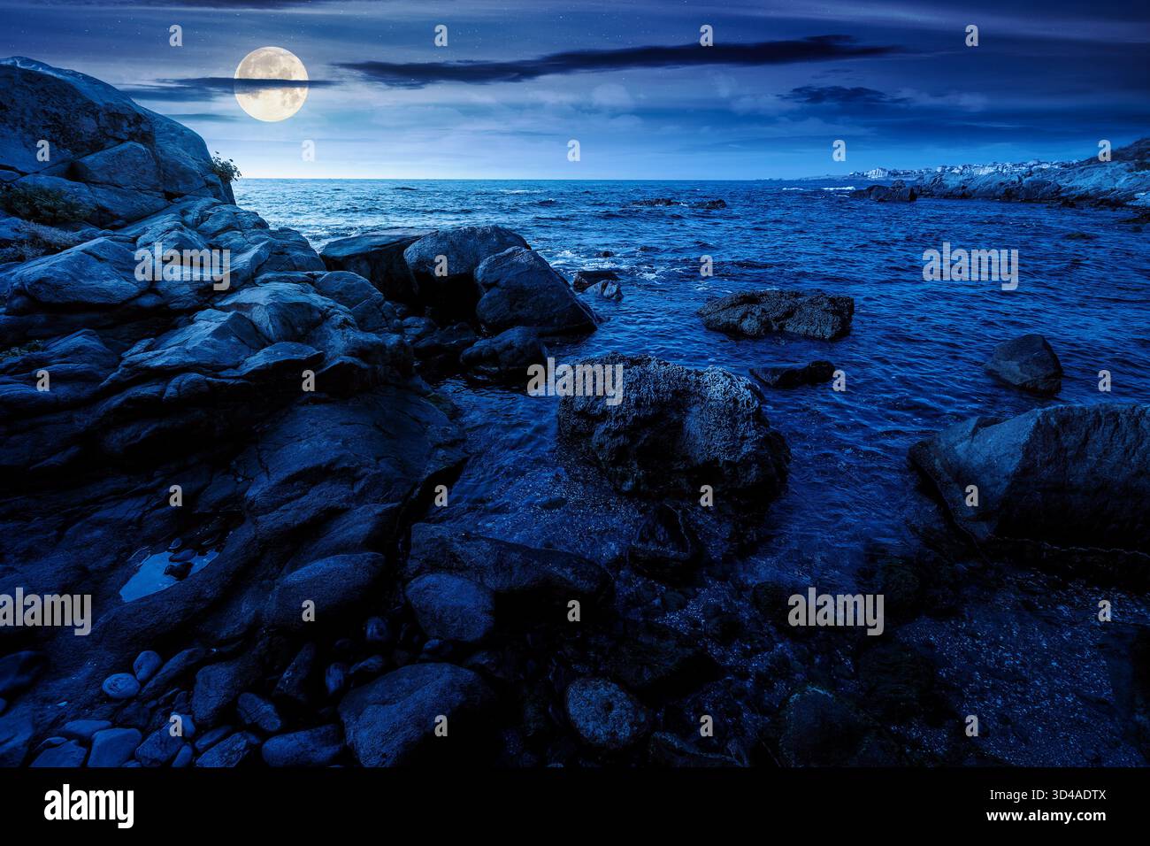 night landscape of rocky sea coast. beautiful full moon over horizon. summer coastline scenic view. composite scene during midnight. magical seascape Stock Photo