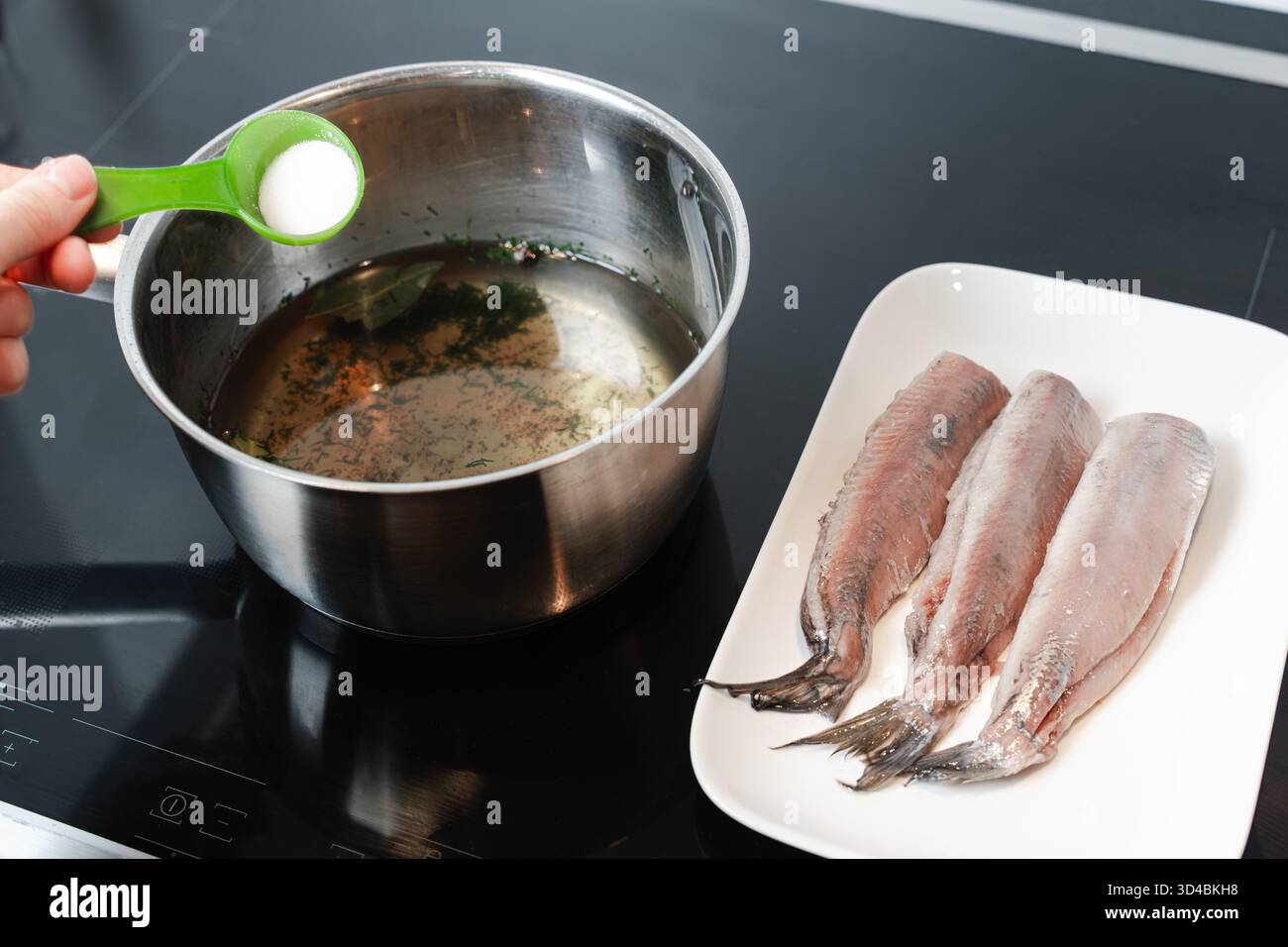 Hand adds salt to aromatic brine for curing raw herring fillets, shown ...