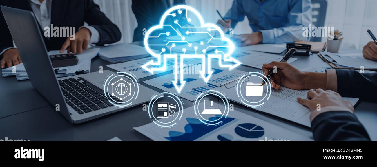 A diverse business team collaborates on cloud computing solutions using laptops and smart devices, surrounded by charts and documents in a modern Stock Photo