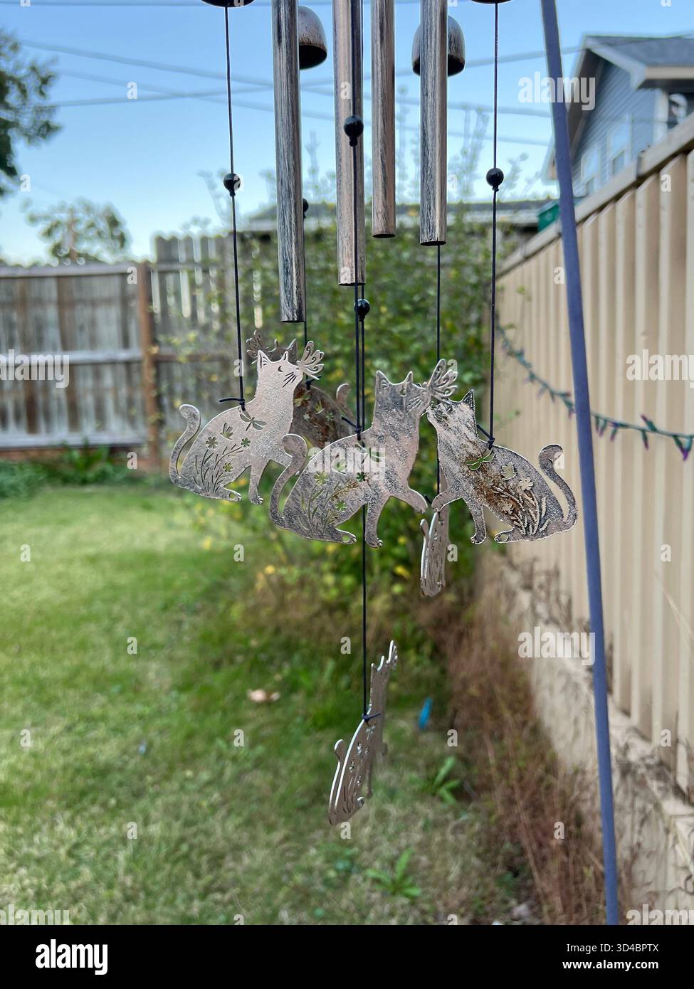 Metal cat wind chime hanging in a backyard garden on a sunny day - Smartphone Captured Stock Image