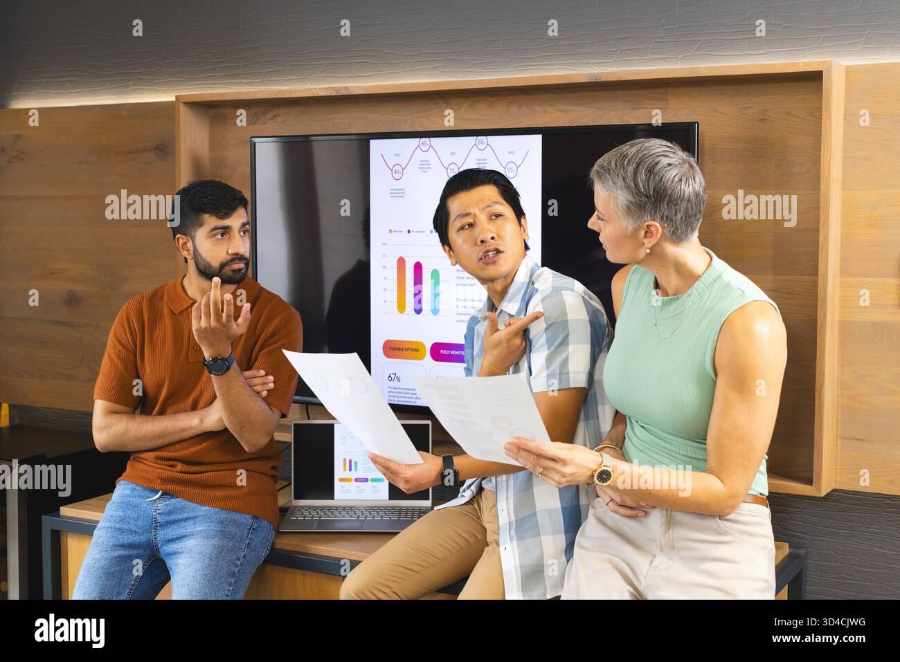 Discussing Diverse coworkers analyzing data on flat-screen at office desk, with printed documents Stock Photo
