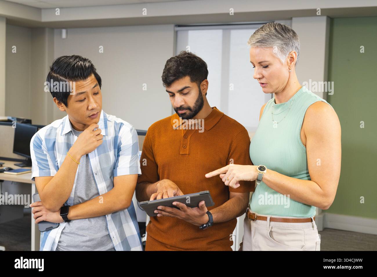 Collaborating instructor with students navigating tablet in computer lab, with desktop computers Stock Photo